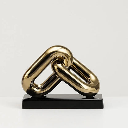 Gold chain-like sculpture on a black base against a light gray background